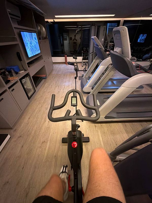 A man and a woman are exercising outdoors, both wearing black sportswear and performing a stretching or warm-up pose on a blue exercise mat.
