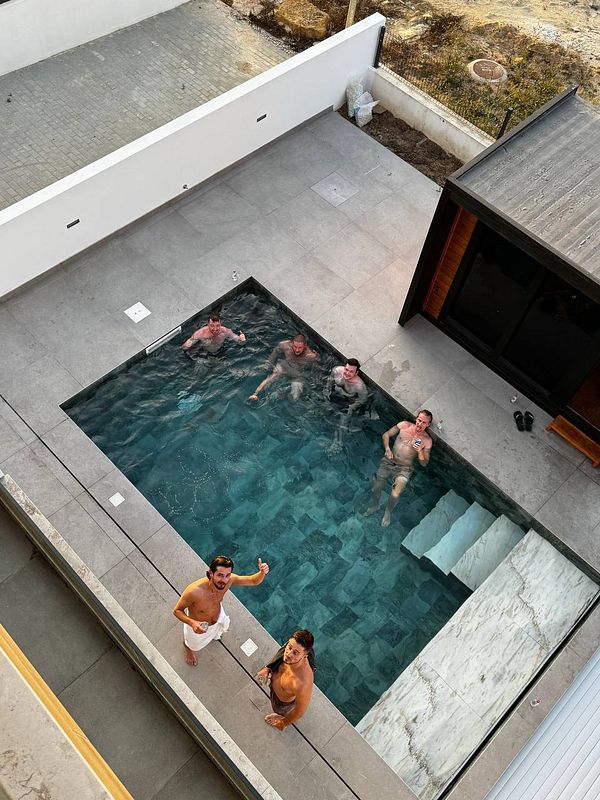 A group of six people are enjoying a swim in a modern pool surrounded by a stylish outdoor area.