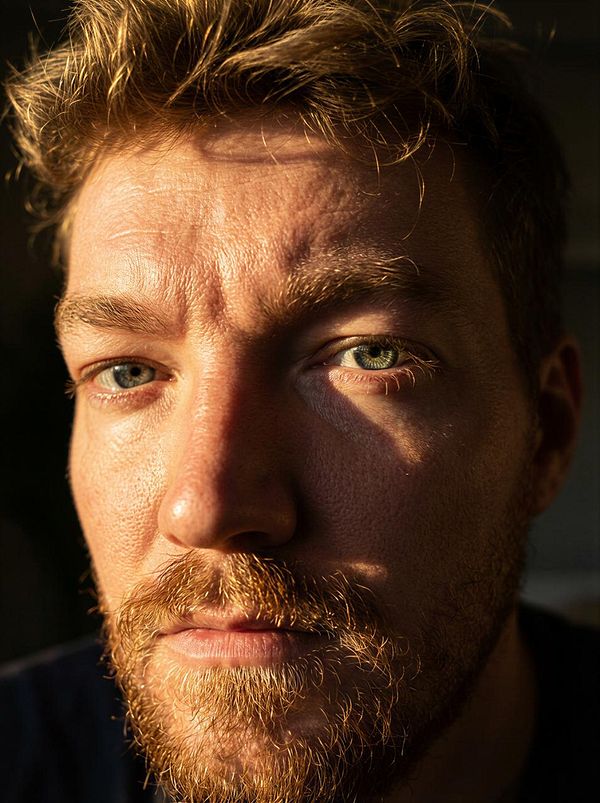 A close-up portrait of a man with a beard, illuminated by natural light.