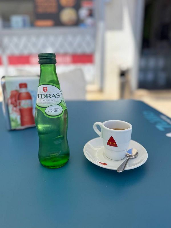 A green bottle of mineral water and a small cup of coffee are placed on a blue table.