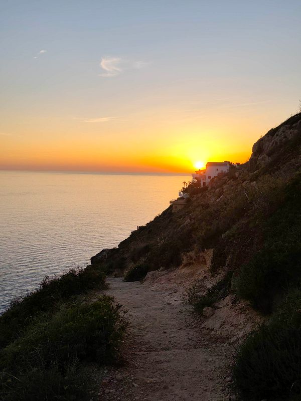 A breathtaking landscape photograph capturing a vibrant sunset over water with silhouetted trees and hills.