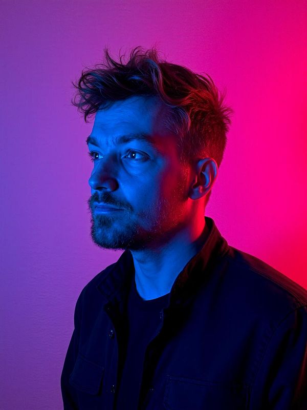 A man is depicted in a striking portrait illuminated by vibrant blue and pink lighting.