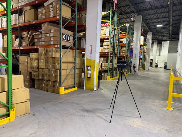 A warehouse interior featuring stacked boxes and a scanning device on a tripod.