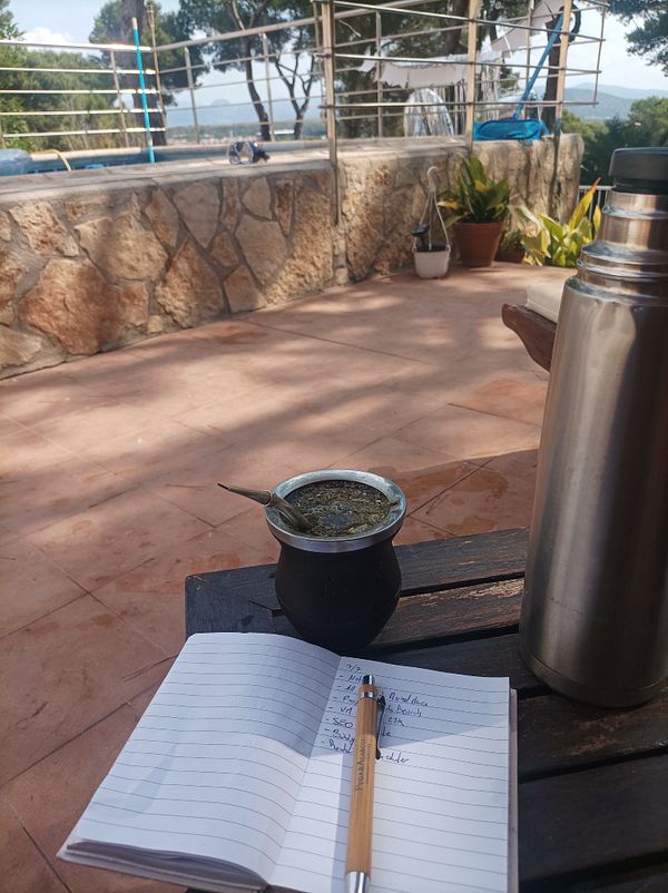 A serene outdoor workspace featuring a notebook, a traditional mate cup, and a thermos.