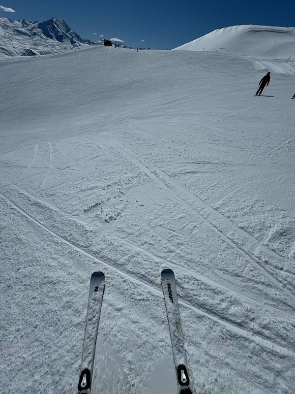 A skier's perspective on a snowy slope with clear blue skies.