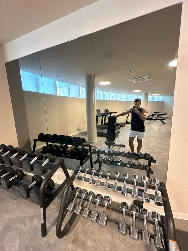 A gym interior featuring dumbbell racks and a person taking a selfie in the mirror.