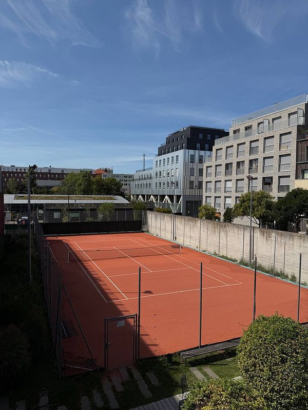 A well-maintained tennis court surrounded by modern buildings and greenery.