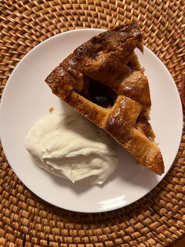 A slice of apple pie served with a dollop of whipped cream on a white plate.