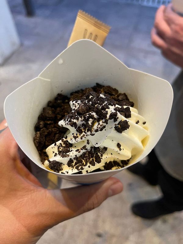 A hand holds a cup of McFlurry topped with crushed cookies and whipped cream.