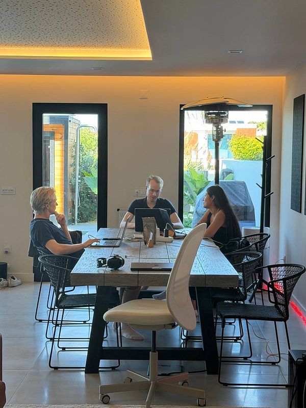 Co-working space with three people working at a large wooden table with laptops and a modern, minimalist interior design.