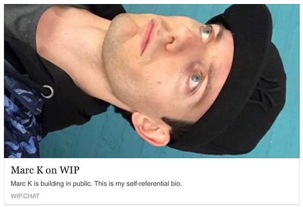 A man with light blue eyes and a black cap is looking upwards against a turquoise background.