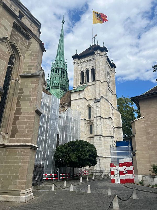The image captures a historic church in Geneva, partially obscured by construction barriers and scaffolding.