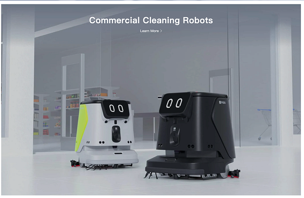 A massive commercial cleaning robot moves down a large industrial corridor in a factory setting.