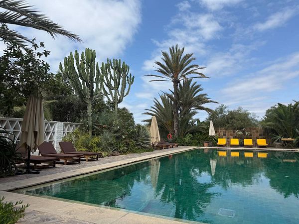 A serene outdoor pool scene in Agadir with palm trees and tranquil blue water under a partly cloudy sky.