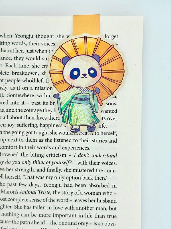 A colorful magnetic bookmark featuring a panda character is placed on a page of a book.