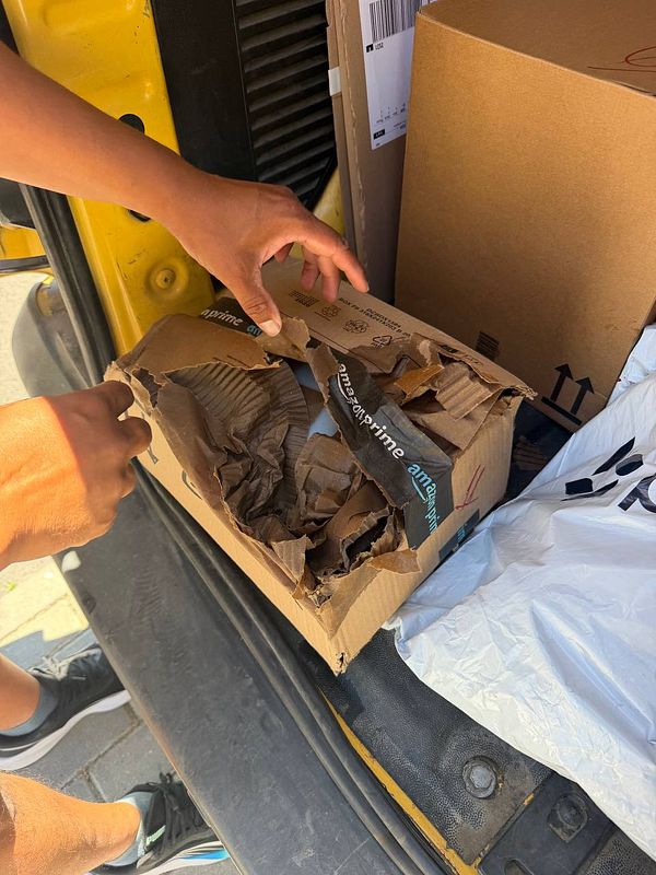 A damaged box labeled 'Windscreen Washer Fluid' that is wet and severely crushed, placed inside a red container.