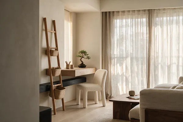 A calm Japandi-style home office with a light wood wall desk, a cream textured chair, and a decorative wooden ladder holding woven baskets. Sheer curtains filter soft daylight over pale floors, while a small bonsai and minimal accessories add a natural, tranquil feel.