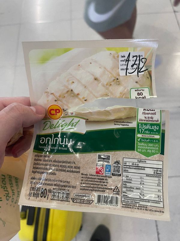 A hand holds a partially opened package of CP Delight Tender Chicken Breast in a shopping area.