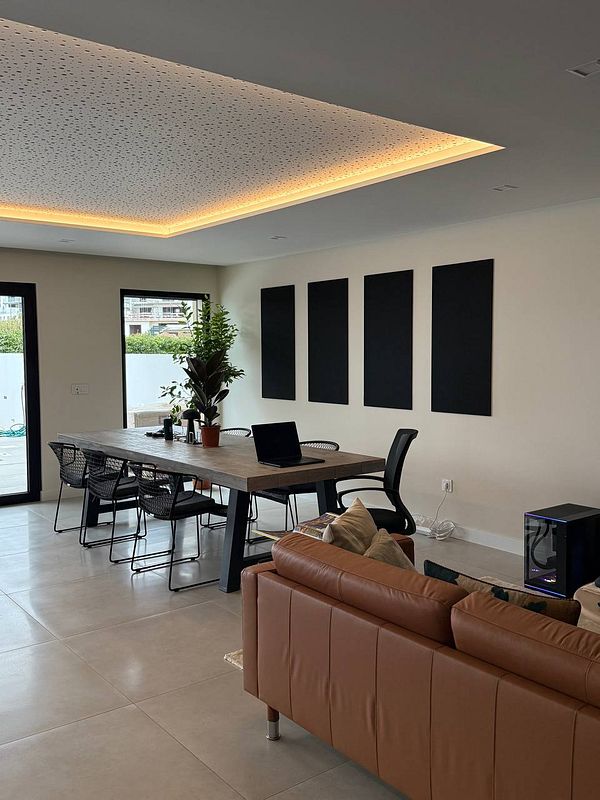 A modern coworking space featuring acoustic tiles, a large dining table, and plants.
