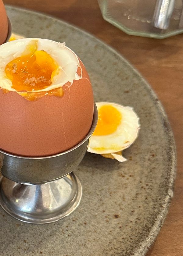 A close-up of soft-boiled eggs served in silver egg cups on a rustic plate.