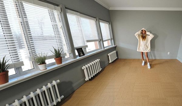 A woman stands in a spacious, well-lit room with large windows and a minimalist design.