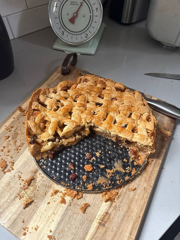 A freshly baked apple pie with a lattice crust sits on a wooden cutting board.
