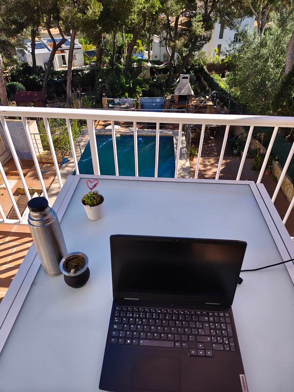 A person working at a wooden outdoor table surrounded by lush greenery under daylight.