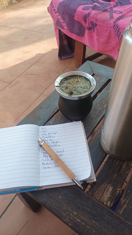 A cozy outdoor workspace featuring a notebook, a mate drink, and a water bottle.