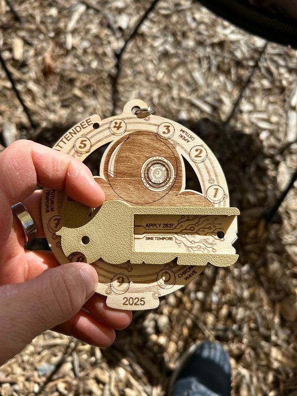 A hand holds a unique wooden badge designed for an event, featuring intricate engravings and a key-like attachment.