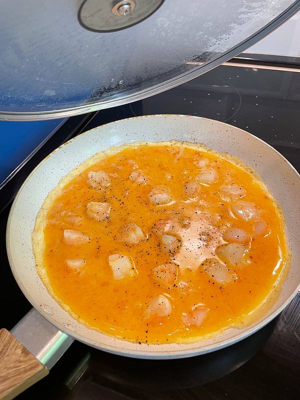 A shrimp omelette is being cooked in a frying pan.