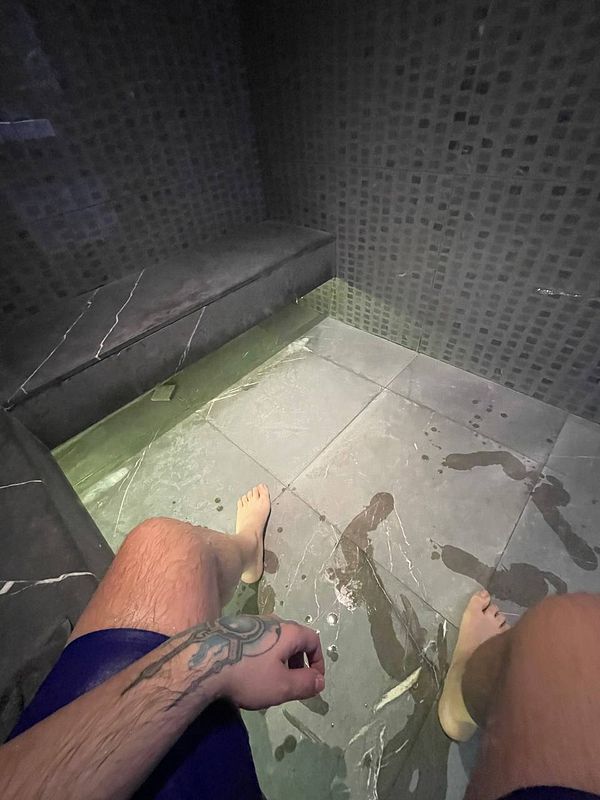A person relaxing in a steam room with water on the floor.