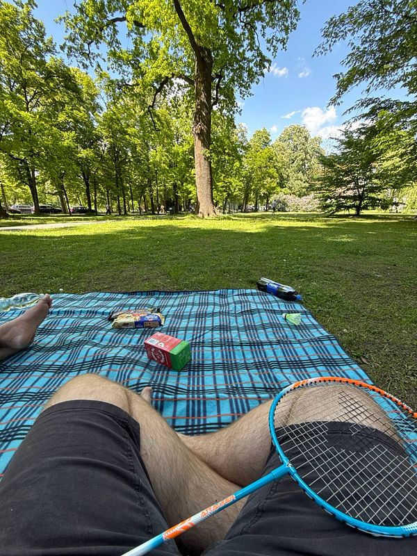 A relaxing scene in a city park featuring a picnic setup and badminton equipment.