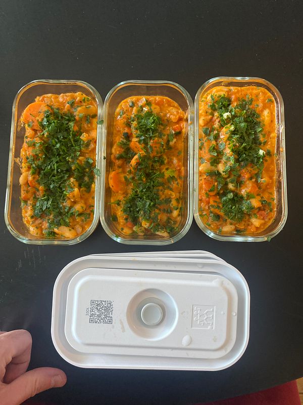 Three glass containers filled with a garnished loubia dish placed next to a plastic lid on a black surface.
