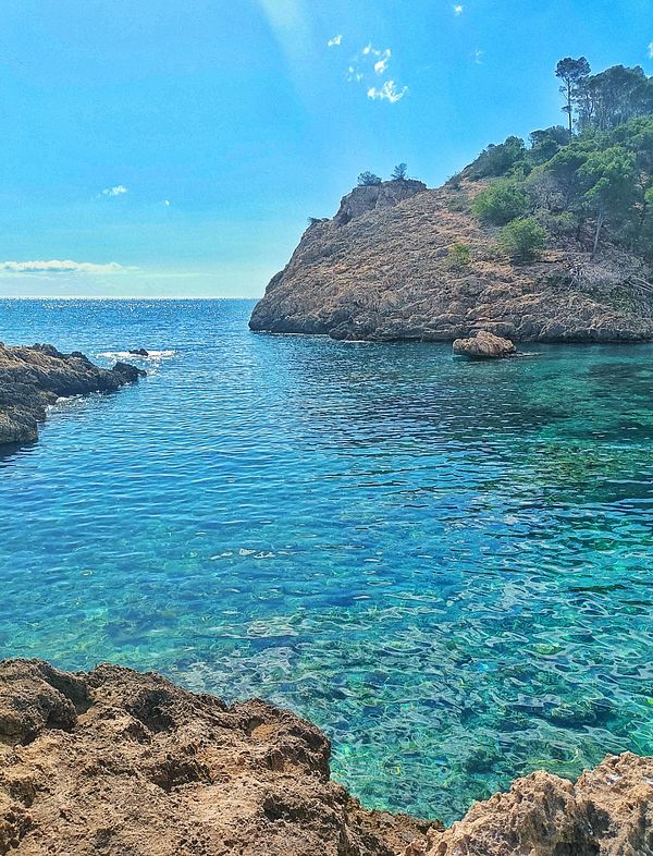 A serene coastal view featuring clear blue waters and rocky cliffs under a bright sky.