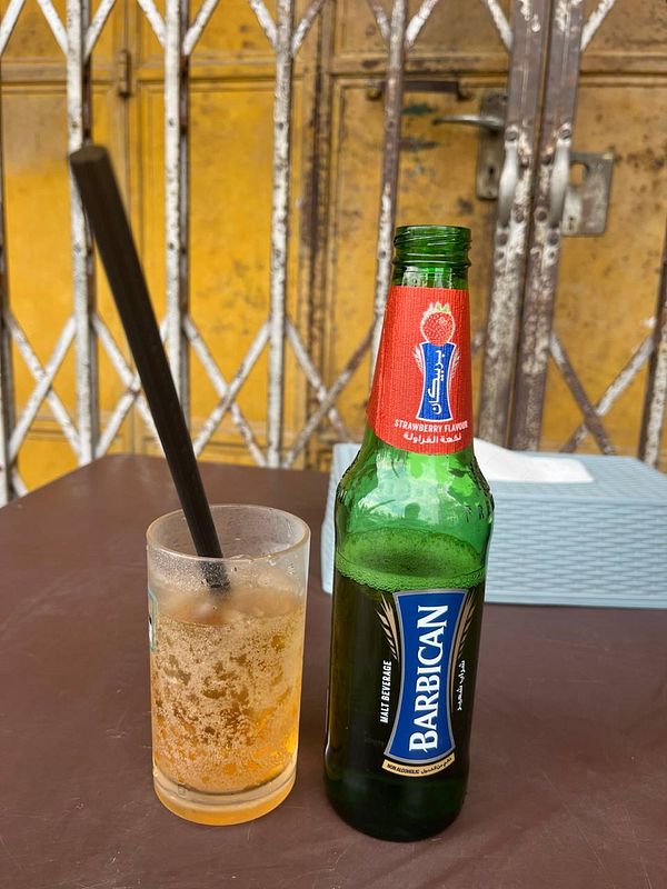 A bottle of Barbican and a glass of a fizzy drink are placed on a table.