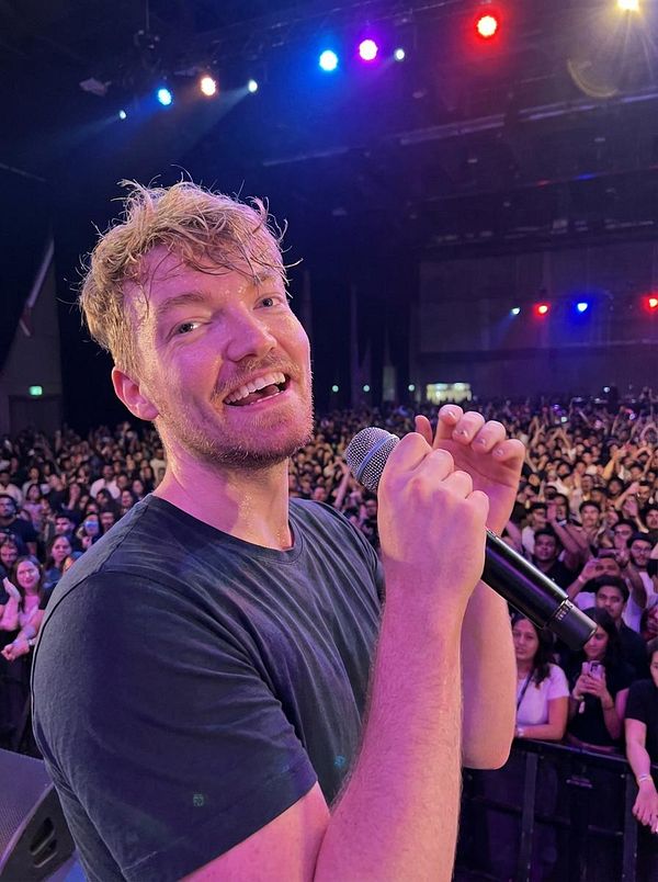 A performer interacts with a large crowd at a concert, holding a microphone and smiling.