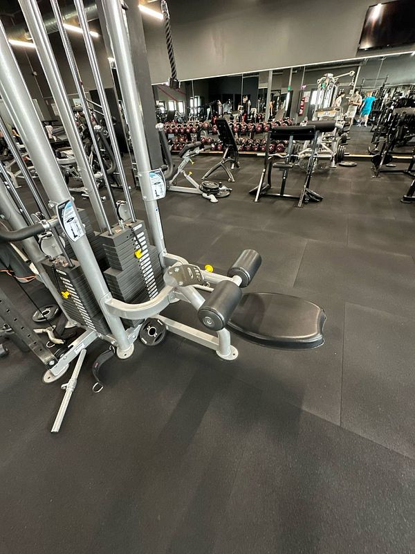 A gym interior featuring various exercise equipment and a focus on a multi-station machine.
