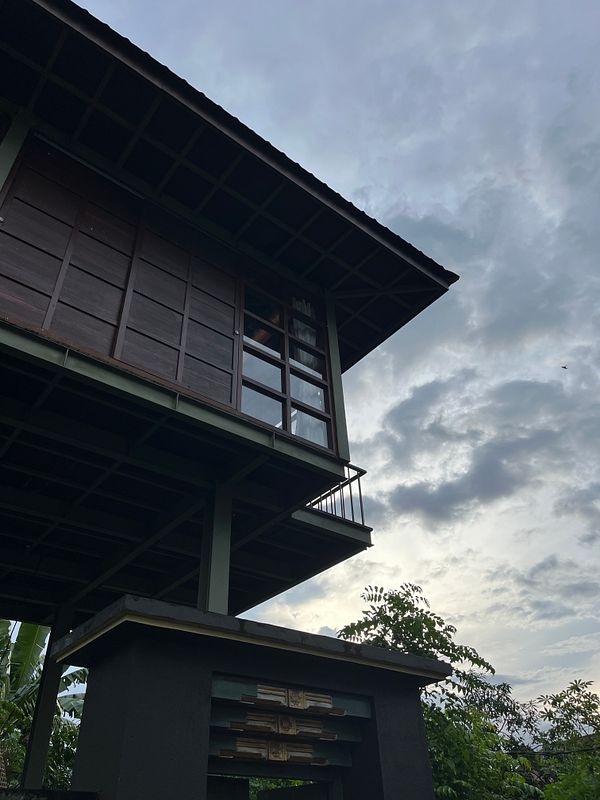 A modern wooden house with large windows is set against a cloudy sky.
