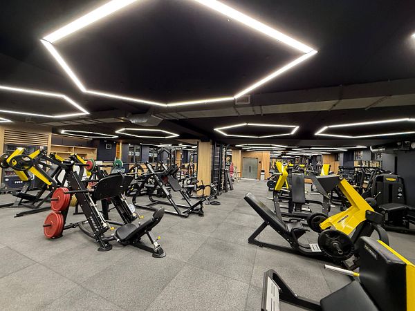 A man lifting weights in a gym with a modern interior that has a mirrored wall and exercise equipment.