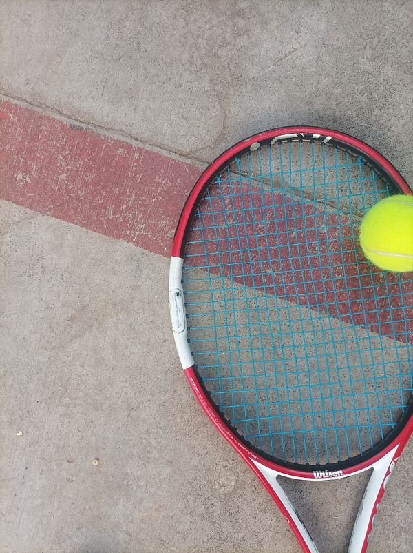 A tennis racket and a bright yellow tennis ball are positioned on a concrete surface.