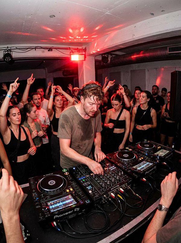 A DJ performs in front of an energetic crowd at a lively music event.