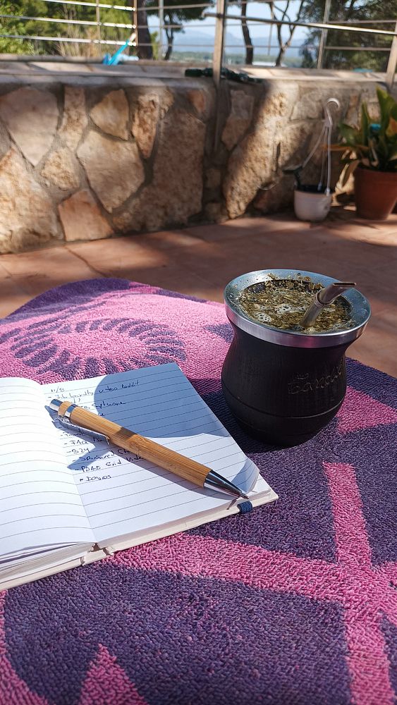 A cozy outdoor workspace featuring a notebook, a pen, and a traditional mate cup.