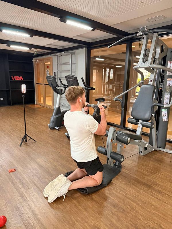A modern gym interior with exercise equipment, a person exercising, and a large mirror wall.