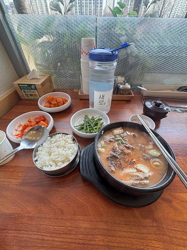 A bowl of sundaeguk, a Korean blood sausage soup, with rice on the side and a metal spoon and chopsticks.