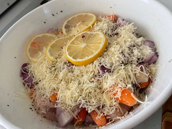 A bowl filled with lemon herb chicken casserole ingredients, topped with cheese and lemon slices.