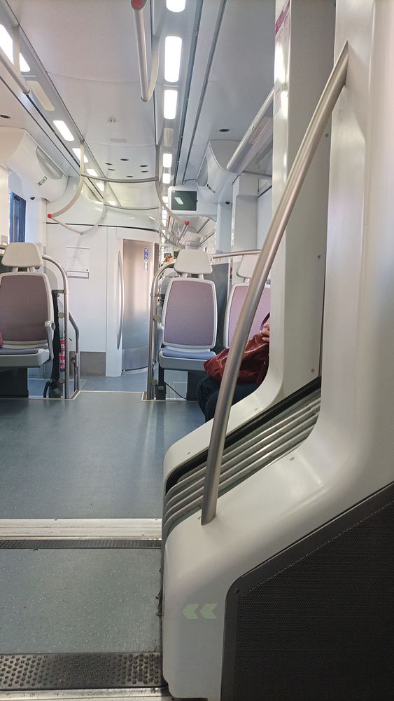 Interior view of a train carriage with empty seats and a passenger.