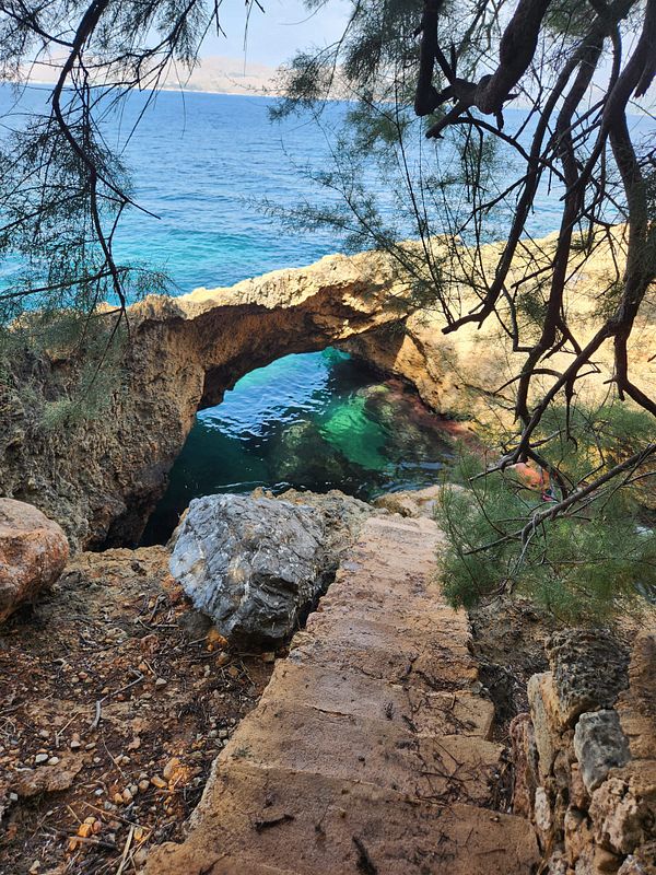 Rocky coastal scene with natural stone arch over clear blue water and stone steps leading down.