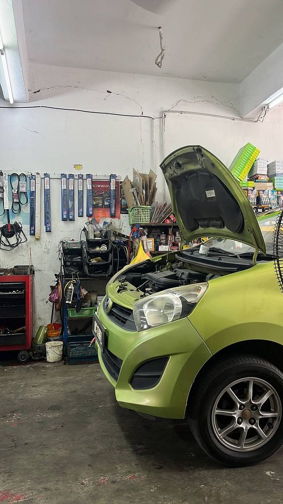 A green car with its hood open is parked in a garage filled with various tools and equipment.