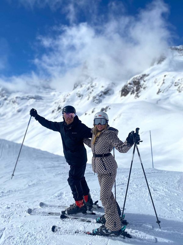 Two skiers pose together on a snowy mountain slope under a clear blue sky.