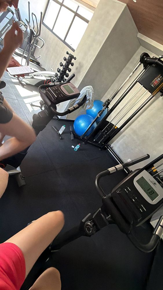 A gym workout setup featuring a floor mirror, dumbbells, a yoga mat, and a speaker in a modern, well-lit room.